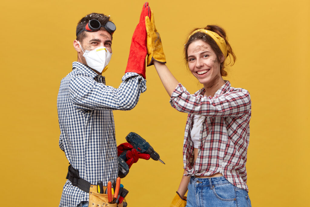 People, occupation, teamwork, cooperation cocncept. Caucasian couple standing sideways doing construction works at home touching their hands together rejoicing their success and great results